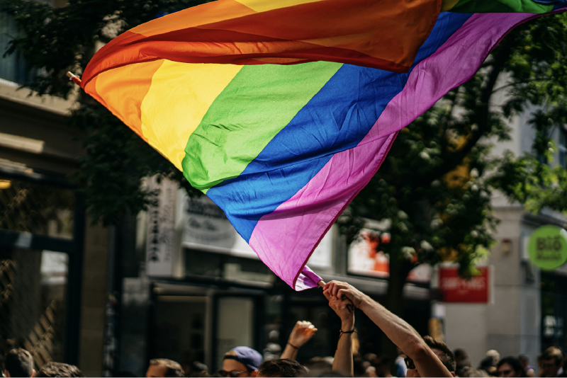 photo of a pride flag being waved over a crowd of people on the street